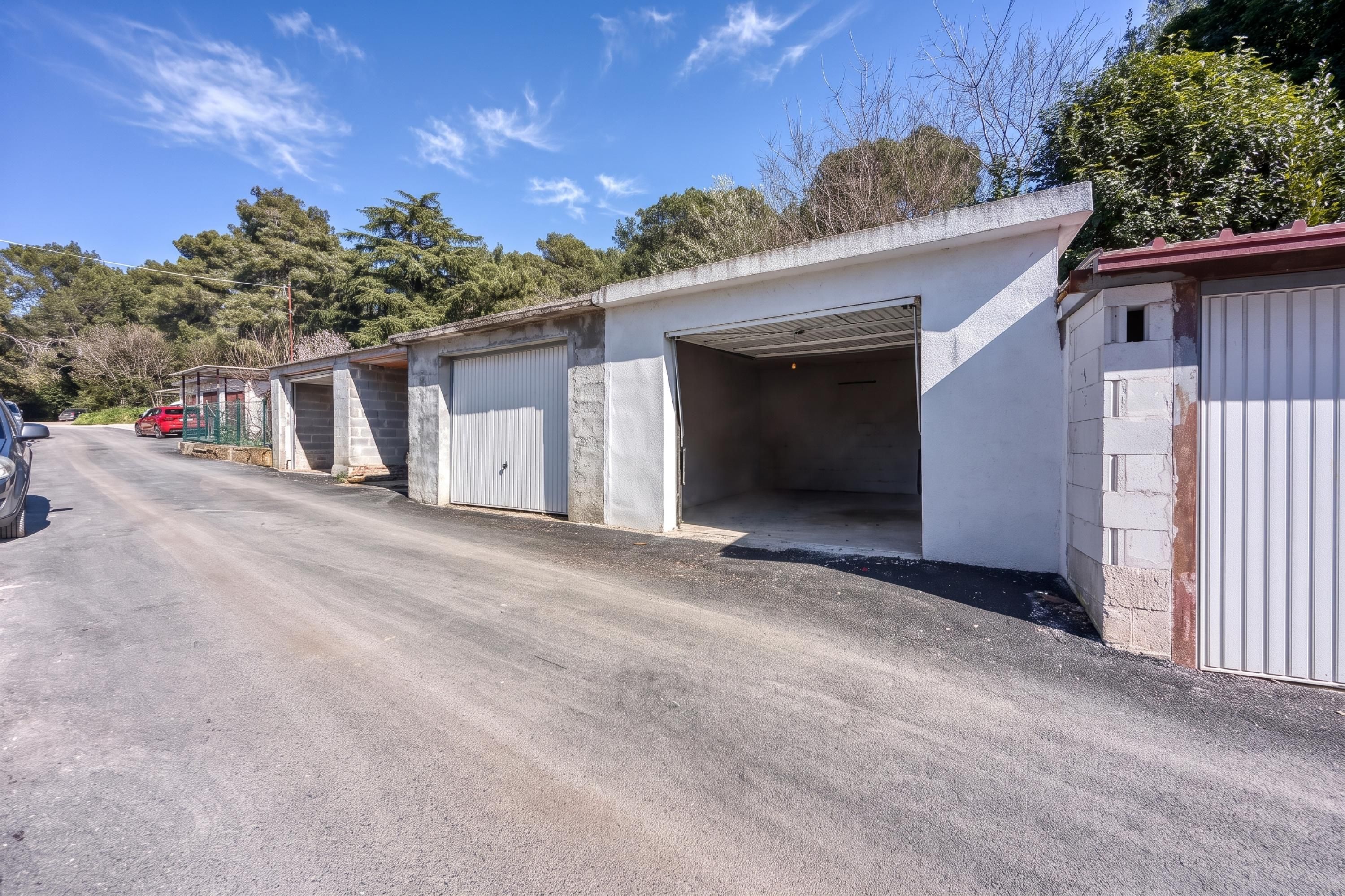 Een rij laagbouwwoningen met open garages, een verharde weg en bomen op de achtergrond.