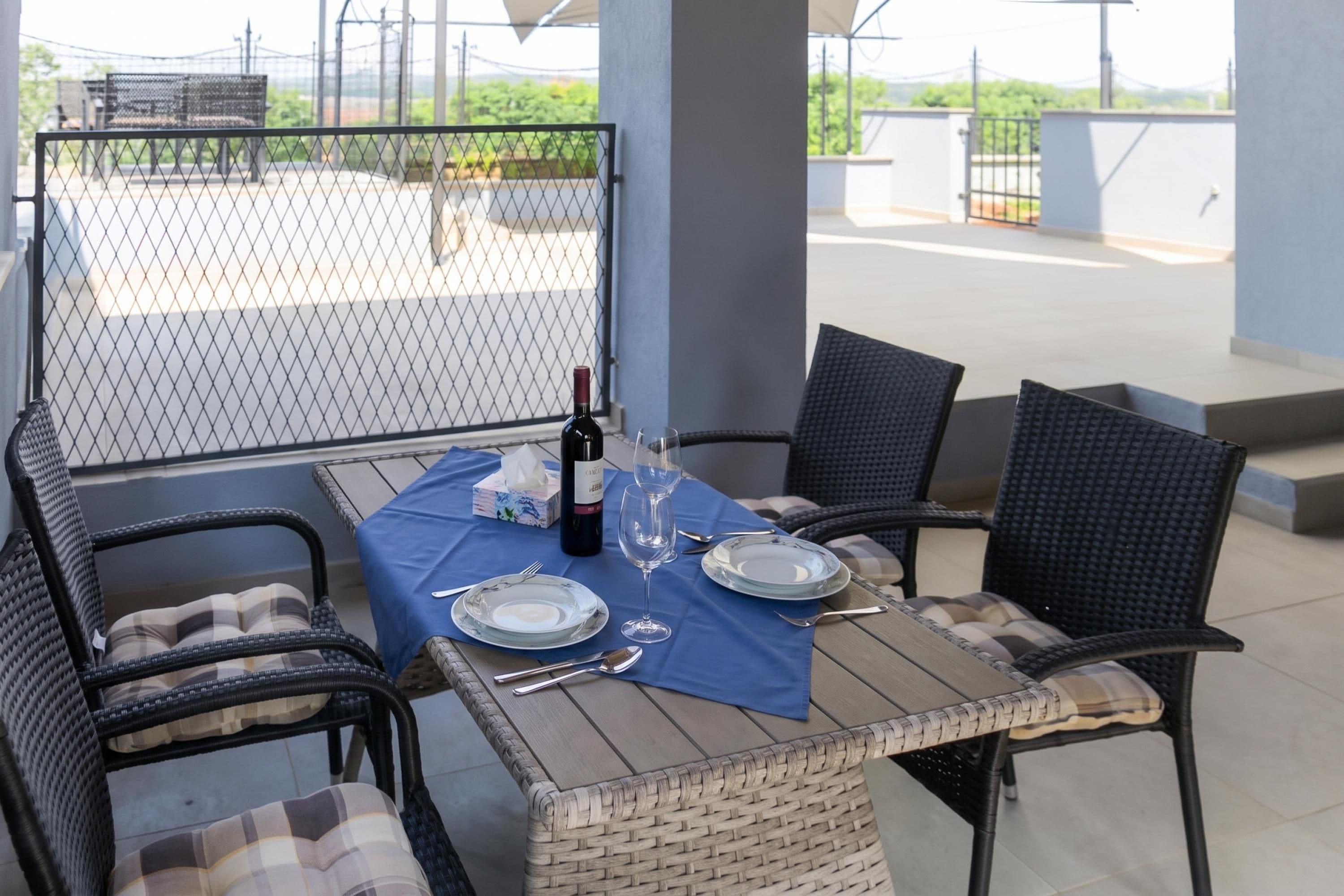 A dining table set outdoors with wicker chairs, a wine bottle, and a glass.