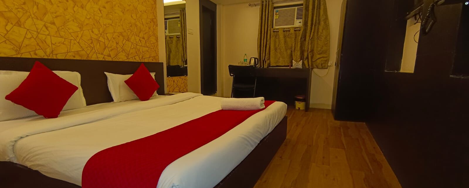 A hotel room with a large bed, a wooden floor, a mirror, and a small table with a chair.