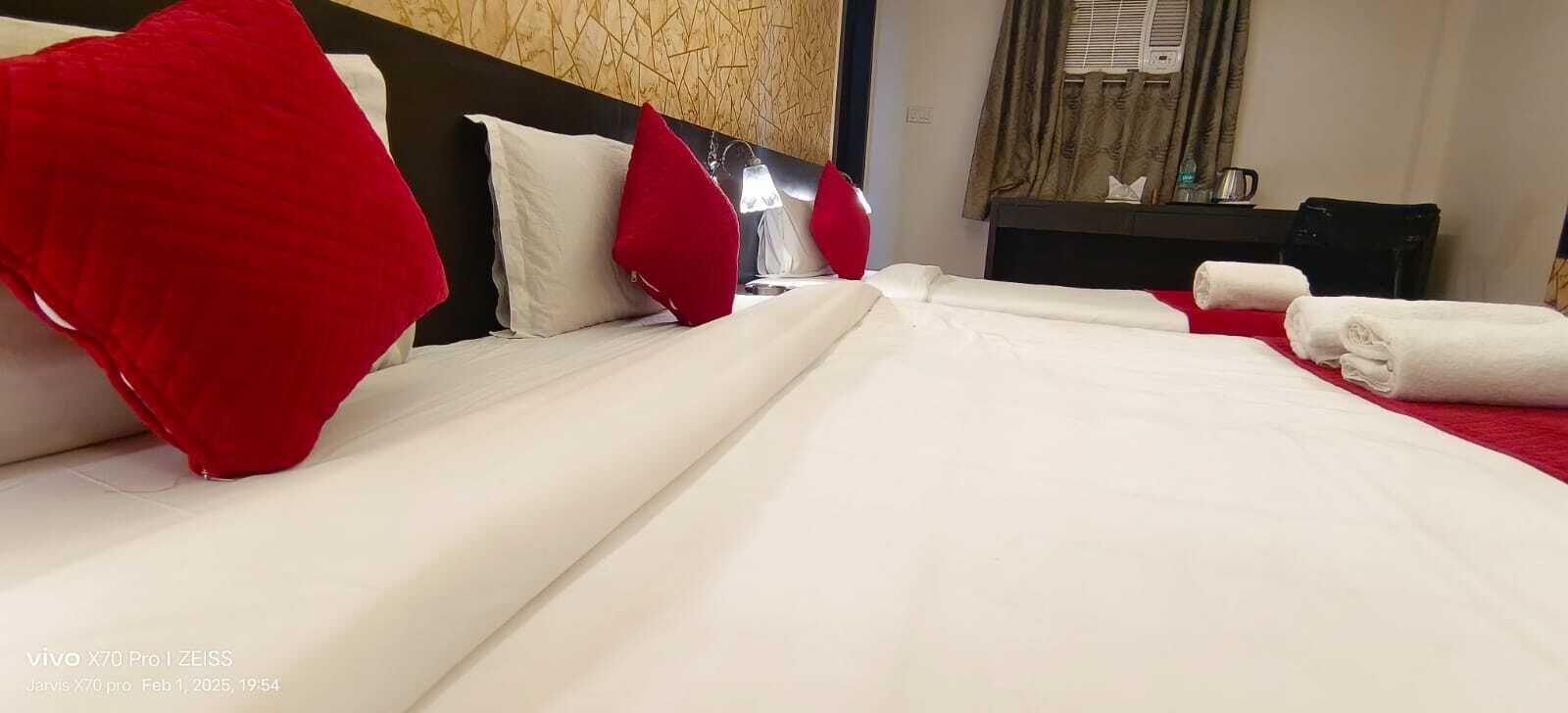 Une chambre d’hôtel avec un lit, des oreillers, une table de chevet, une lampe et une fenêtre avec des rideaux.