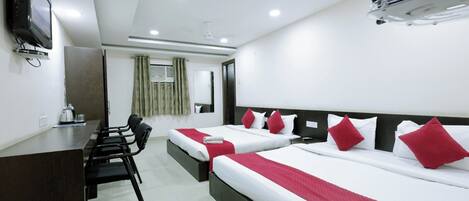 A hotel room with two beds, a desk, a chair, a TV, and a ceiling fan.