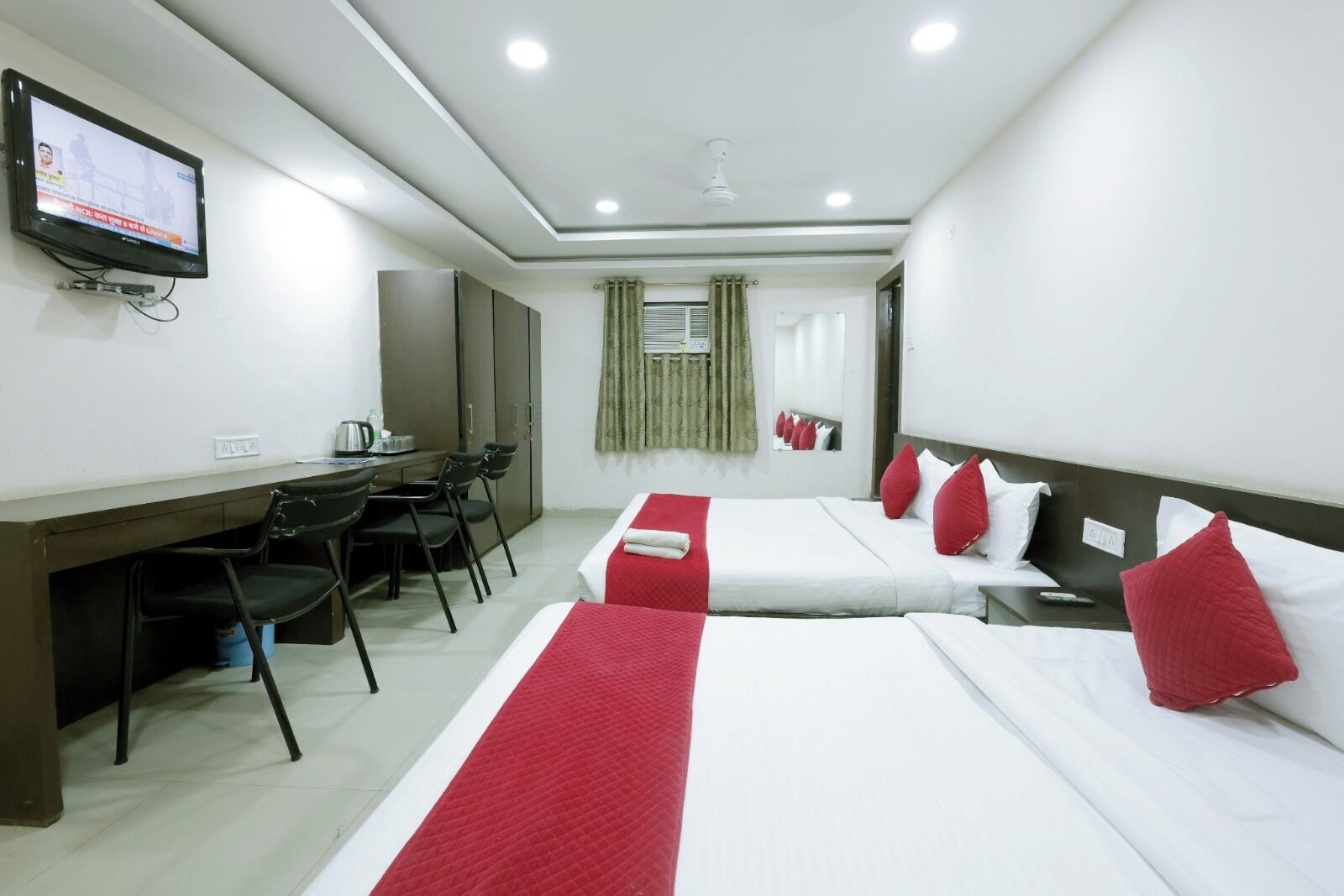 A hotel room with two beds, a desk, chairs, a television, and a window with curtains.