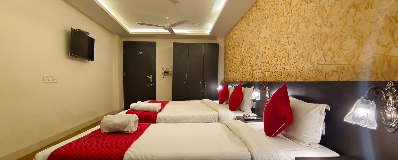 A hotel room with two beds, a ceiling fan, a TV, and a patterned wall.