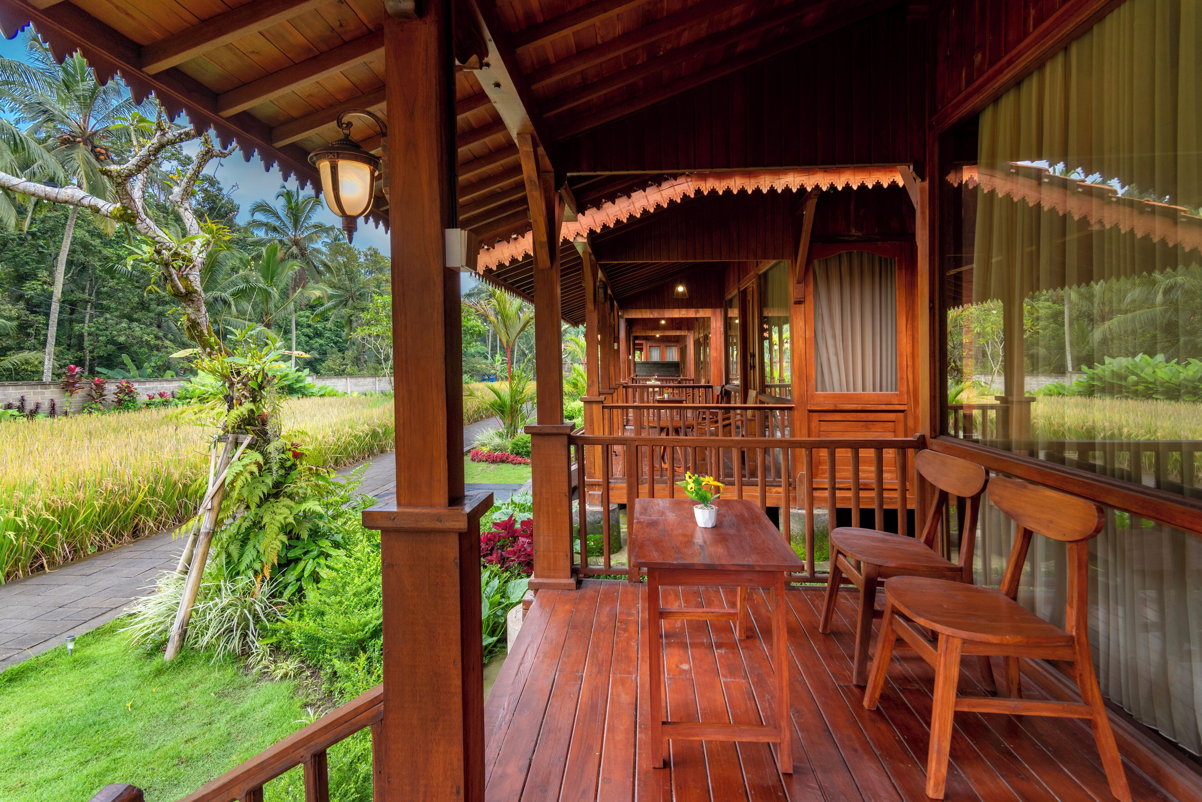 A wooden deck with a table and chairs, surrounded by lush greenery and a view of a tropical landscape.