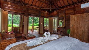 A wooden room with a large bed, a wooden desk, and a view of greenery outside.