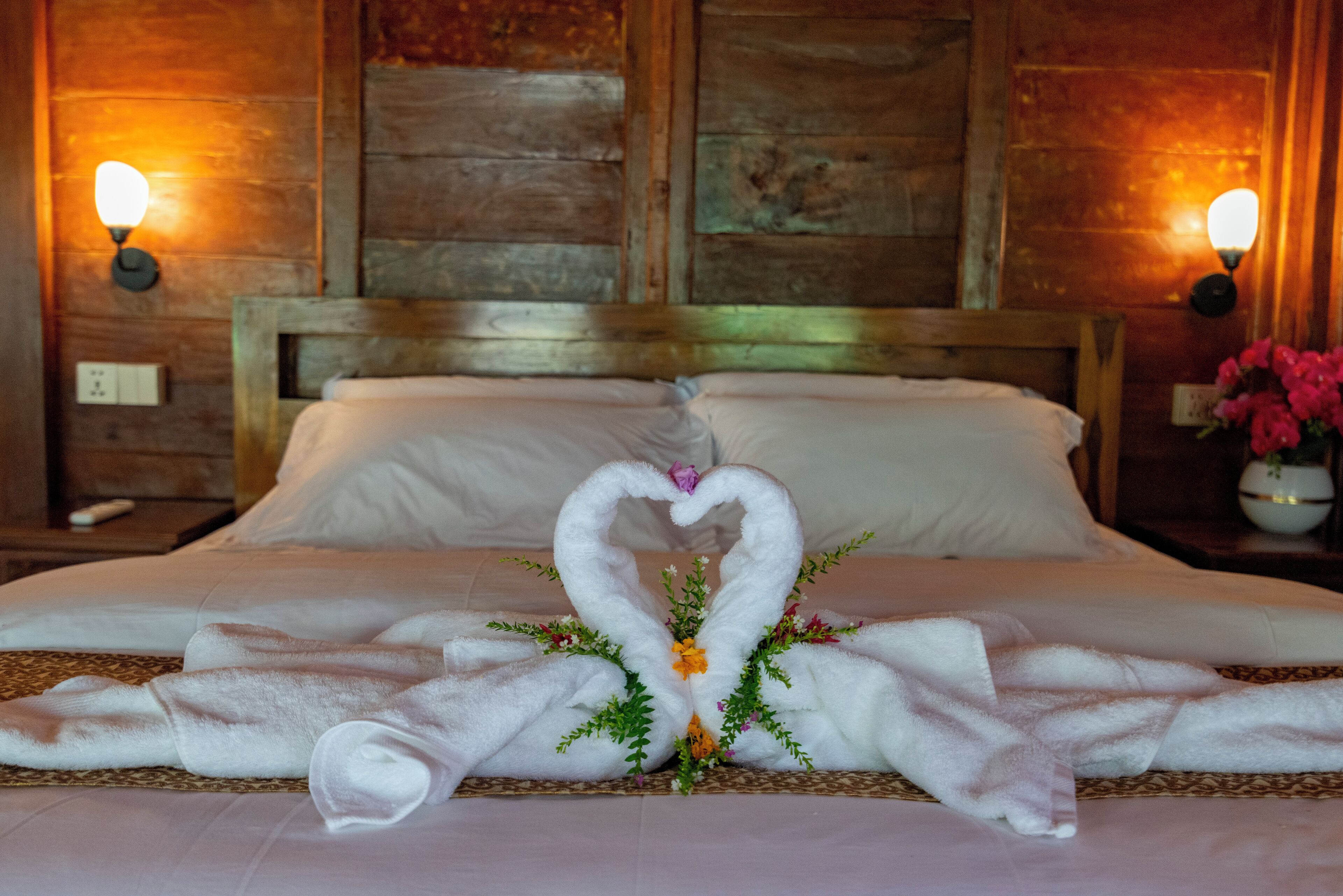 A bed with a heart-shaped towel arrangement and a decorative plant.