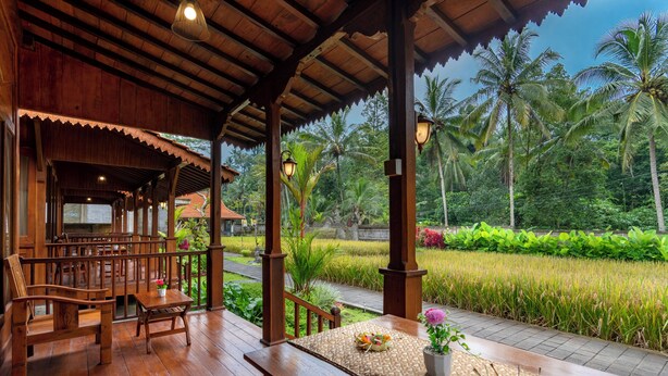 A wooden deck with a table and chairs, overlooking a lush garden and rice field.