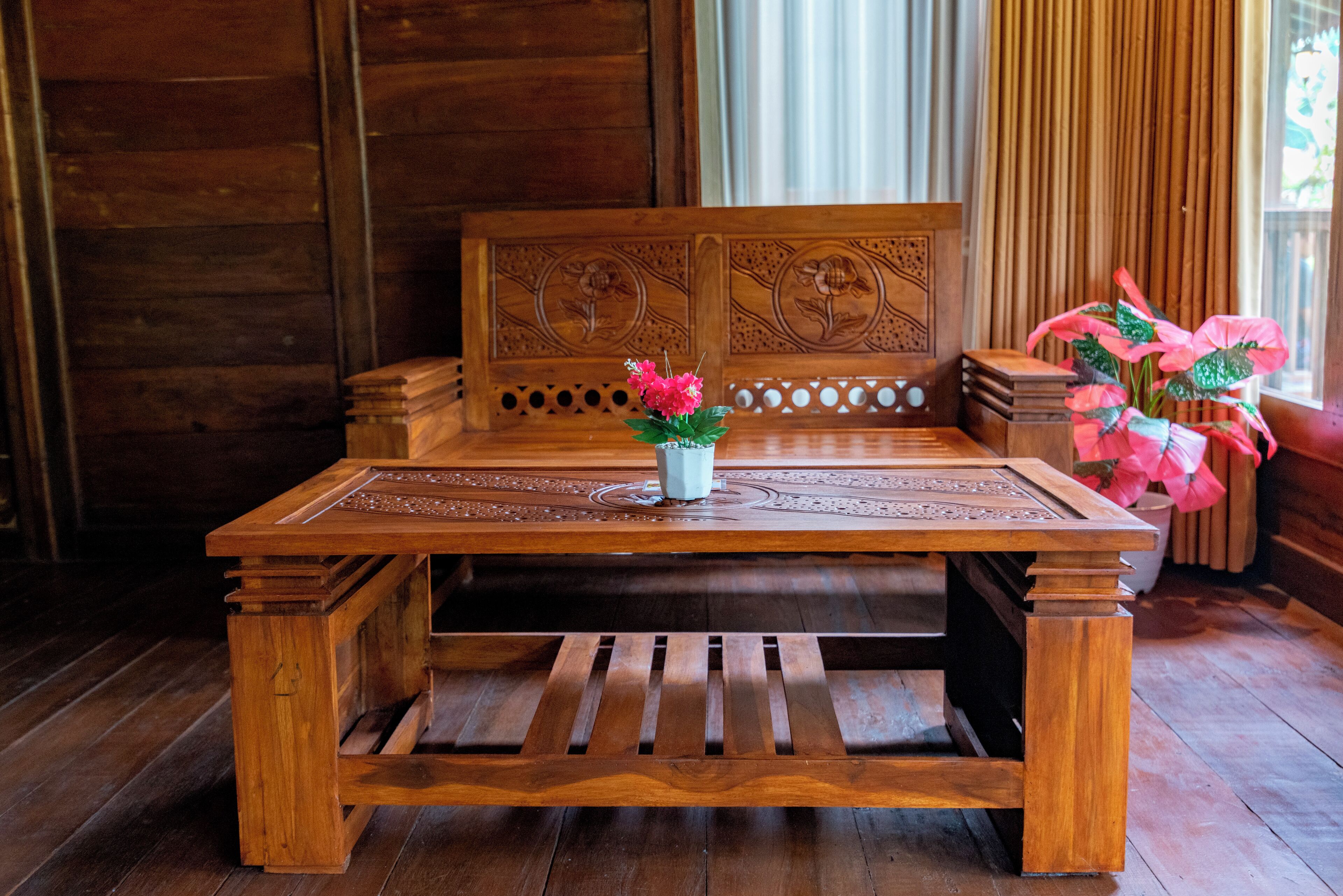 Una mesa de madera con tallas intrincadas, un jarrón con flores rosadas y un banco de madera con detalles florales.