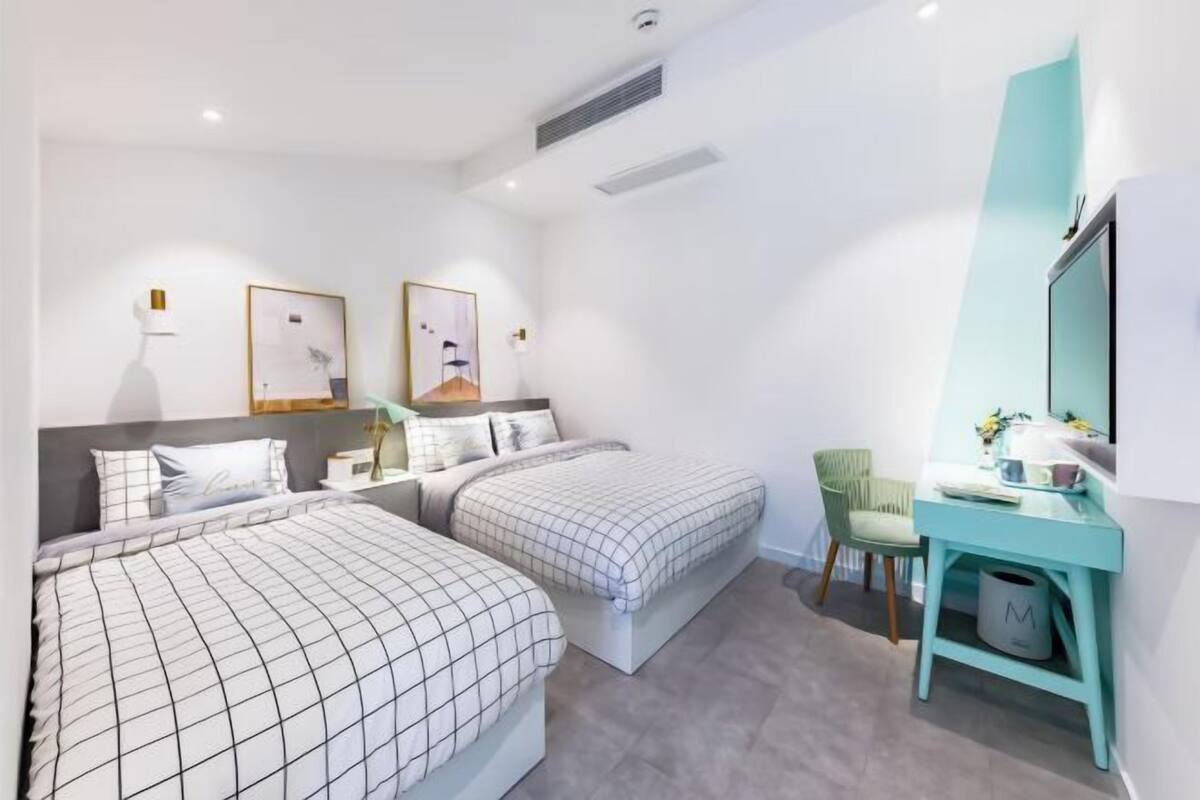 A modern hotel room with two beds, a desk, a chair, and a large mirror.