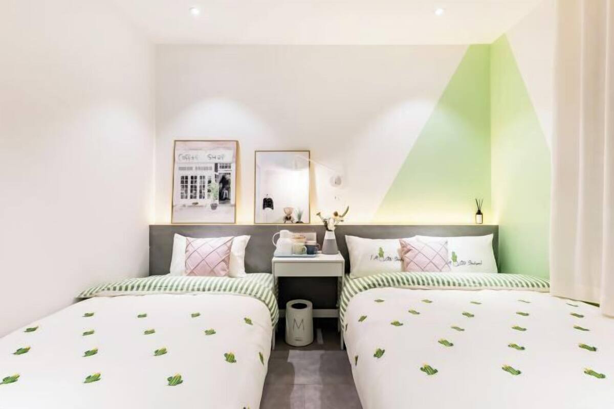 A hotel room with two beds, a nightstand, a mirror, and a green accent wall.