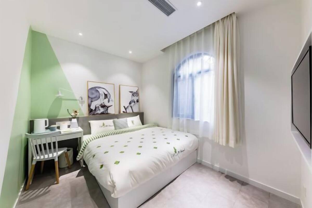 A bedroom with a bed, a desk, and a chair. There are two framed pictures on the wall.