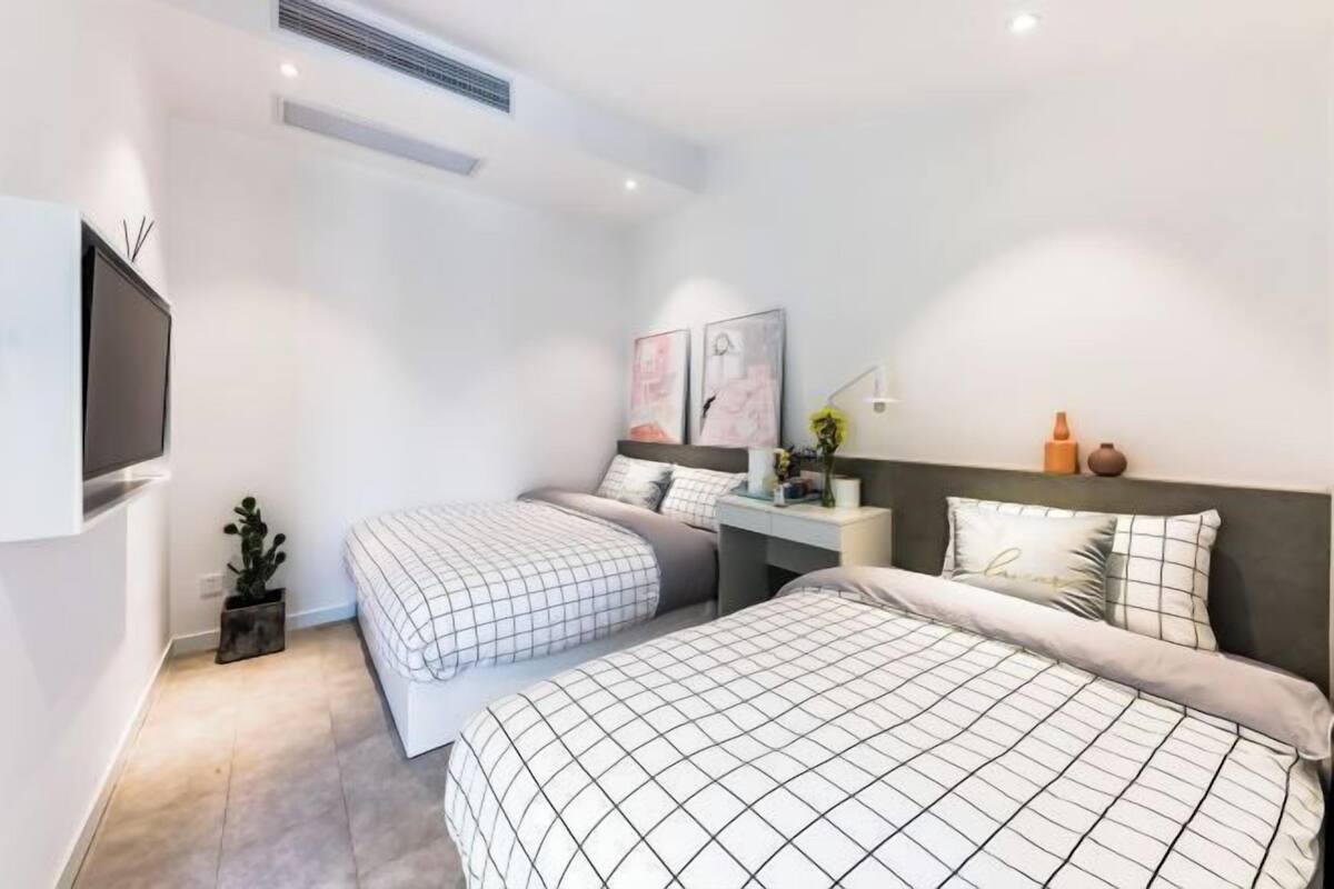 A modern bedroom with two beds, a flat-screen TV, a desk, and artwork on the walls.
