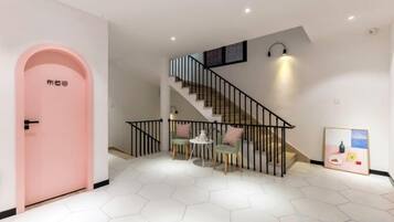 A staircase with a black railing leading to an upper floor, a pink door on the left, and a hexagonal tiled floor.