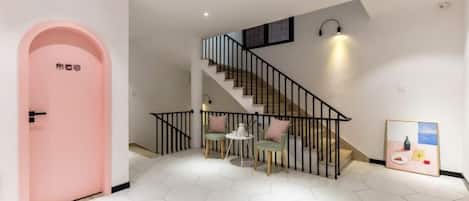 A staircase with a black railing leading to an upper floor, a pink door on the left, and a hexagonal tiled floor.