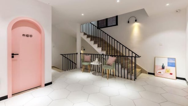 Un interior moderno con una escalera, una puerta rosa y pavimento hexagonal.