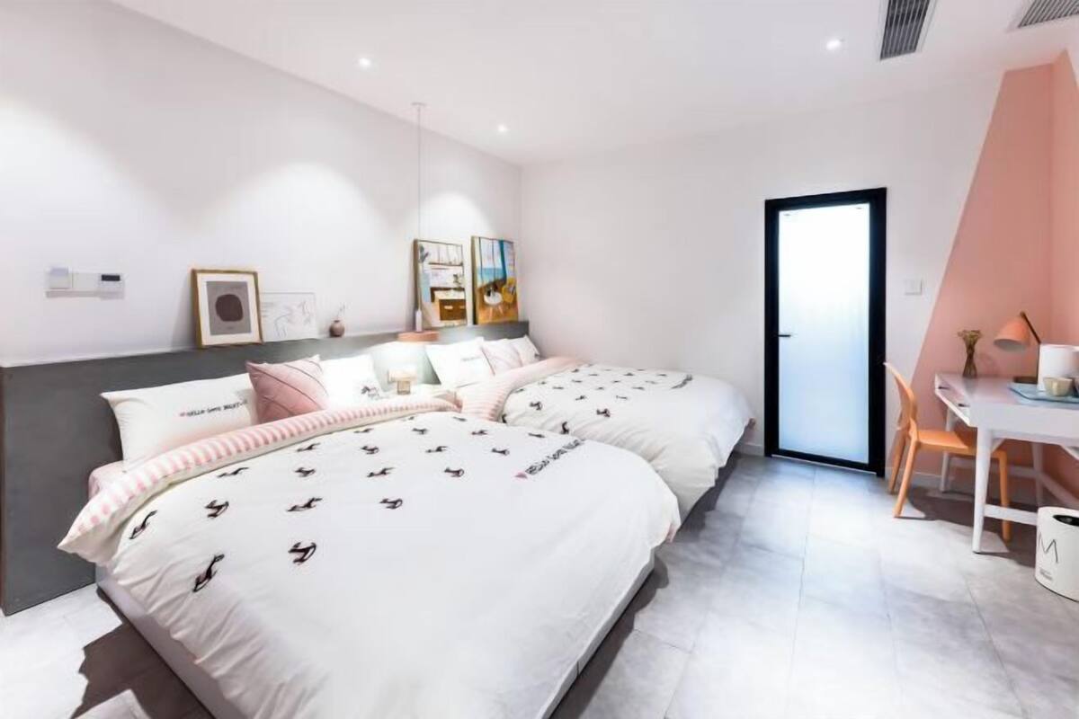 A modern bedroom with two beds, a desk, and a chair.
