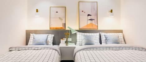 A hotel room with two beds, a nightstand, and wall-mounted lamps.