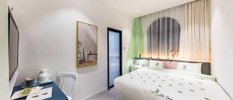 A modern hotel room with a bed, a desk with a chair, a radiator, and a painting on the wall.