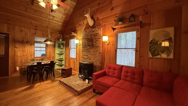 A cozy cabin interior with a dining area, a fireplace, a red sofa, and wooden walls. - Cabin, Hot Tub, Forest View, Close to Town (West Jefferson)