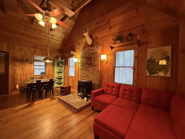 A cozy cabin interior with a dining area, a fireplace, a red sofa, and wooden walls. - Cabin, Hot Tub, Forest View, Close to Town (West Jefferson)