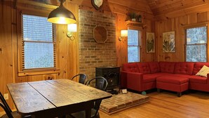 A cozy cabin interior with a wooden dining table, red sectional sofa, and a brick fireplace. - Cabin, Hot Tub, Forest View, Close to Town (West Jefferson)