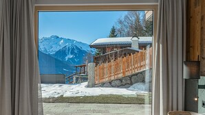 A bedroom with a large window overlooking a snowy mountain landscape, a wooden staircase, and a stone wall.