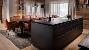 A modern kitchen with a central island, wooden walls, and a dining area with leather chairs.