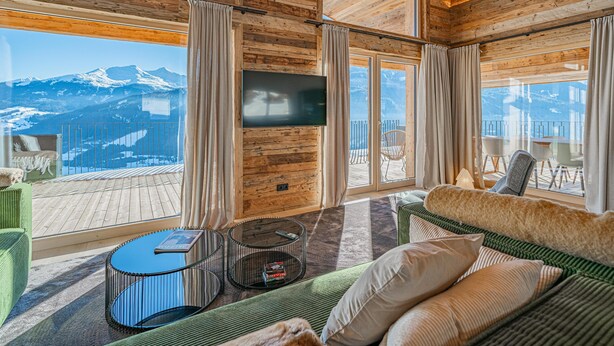A cozy room with a wooden ceiling, a large TV, and a view of snow-capped mountains.