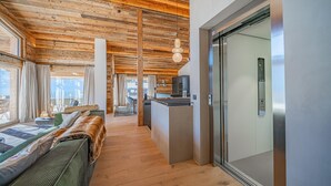 A modern interior with wooden ceiling beams, a sofa, a dining area, and a kitchen with a refrigerator.
