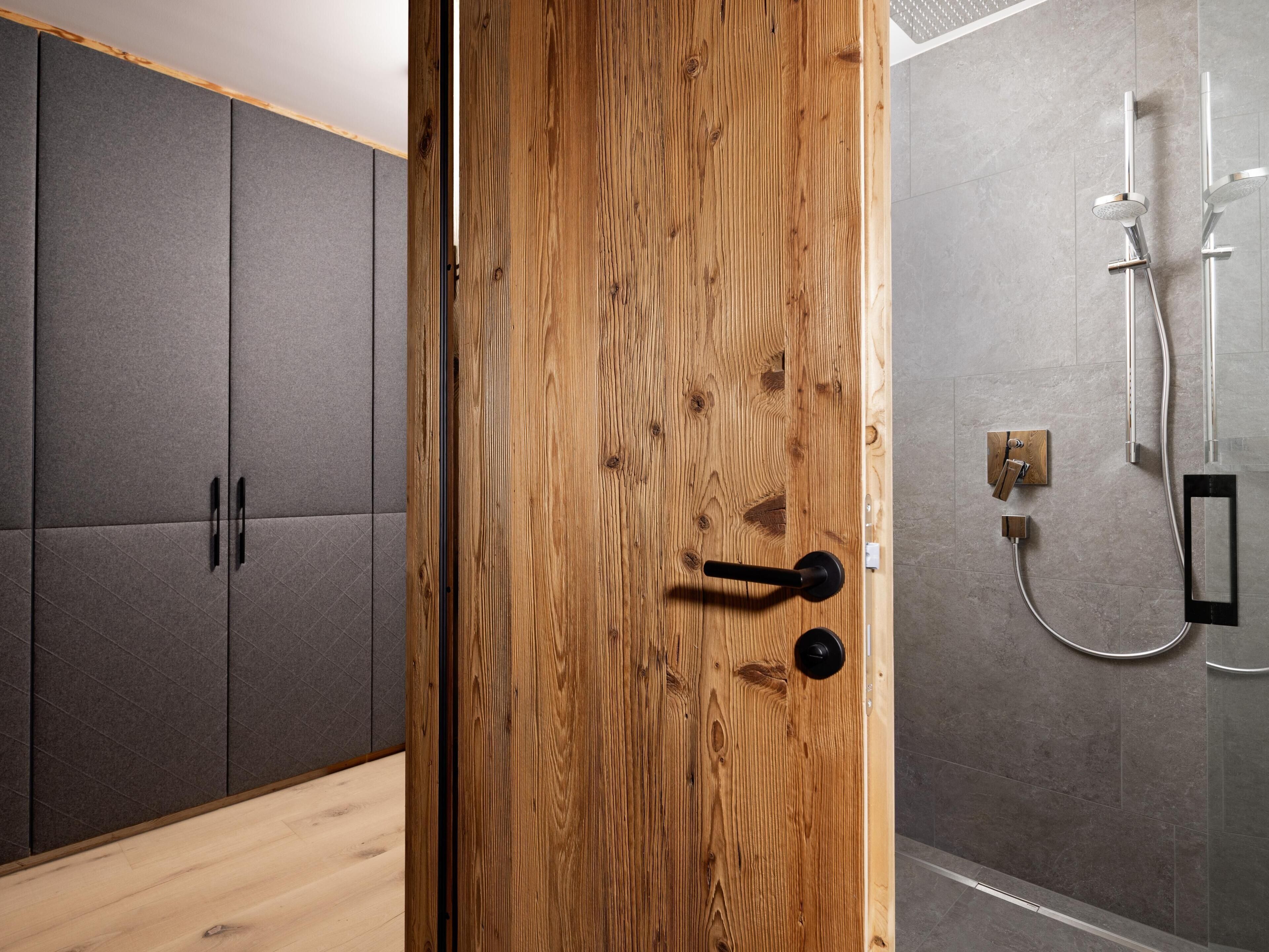 A modern bathroom with a wooden door, grey cabinets, and a shower area.