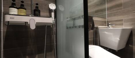 A modern bathroom with a glass shower enclosure, a white toilet, and a shelf with toiletries.