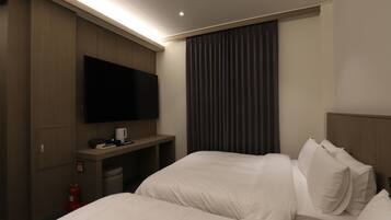 A hotel room with two beds, a flat-screen TV mounted on the wall, a small desk with a coffee maker, and a fire extinguisher.