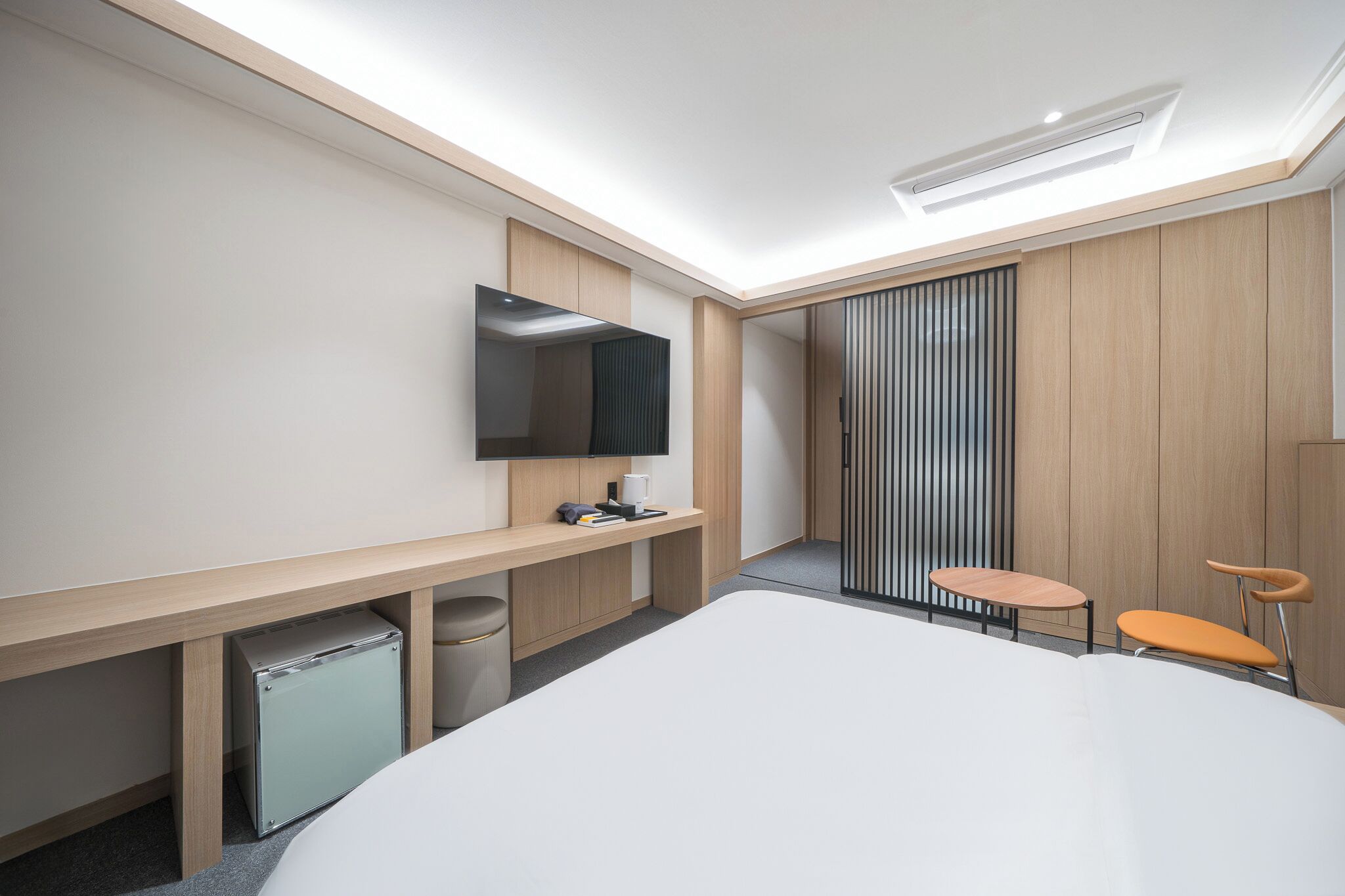 A modern hotel room with a large bed, a desk, a chair, a TV, and a sliding door.