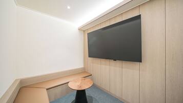 Een moderne kamer met een groot flatscreen-televisie aan de muur, een houten bankje en een klein rond tafeltje.