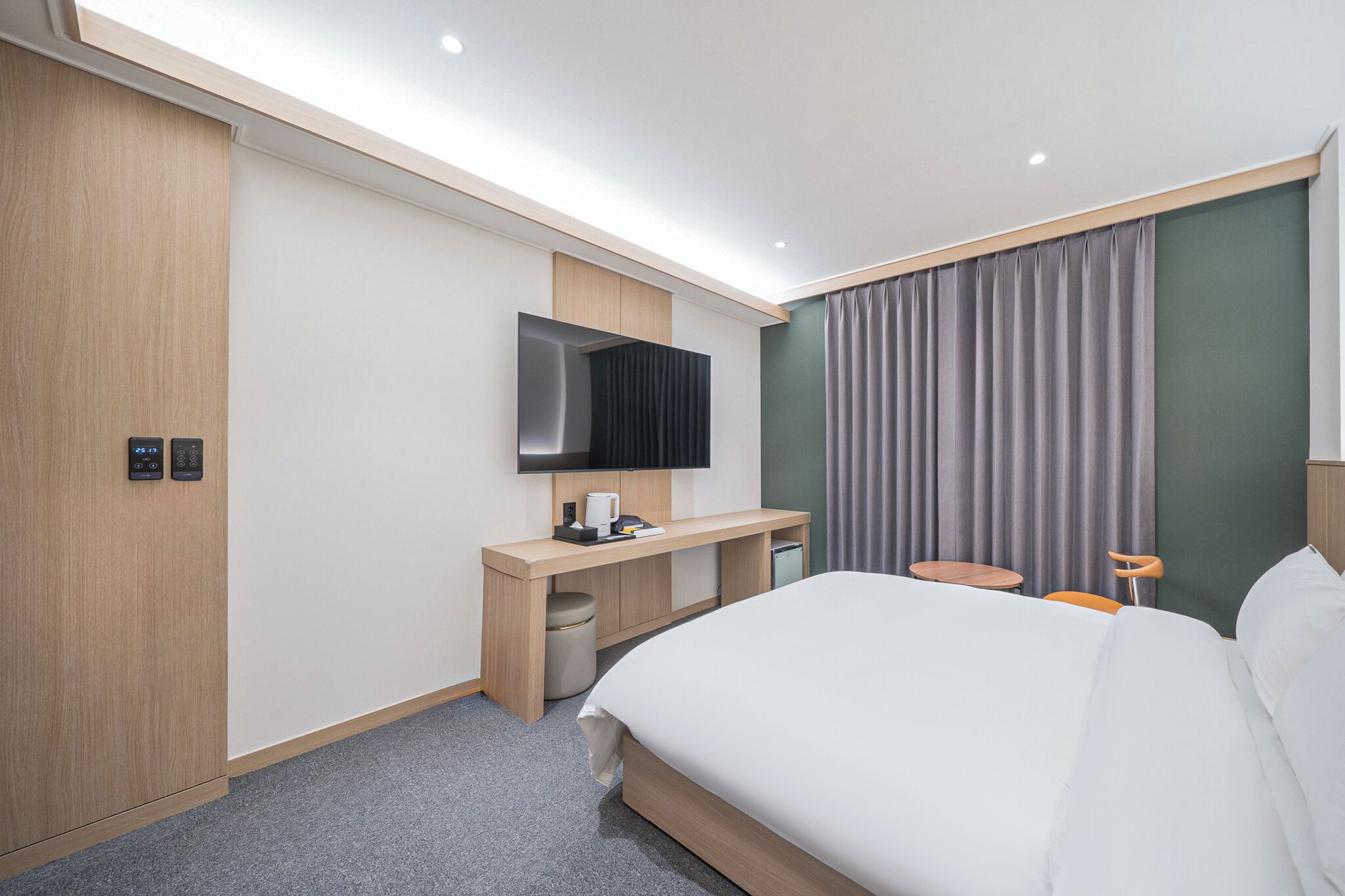Una camera d'albergo moderna con un ampio letto, una scrivania con TV a schermo piatto, un tavolino e una poltrona.