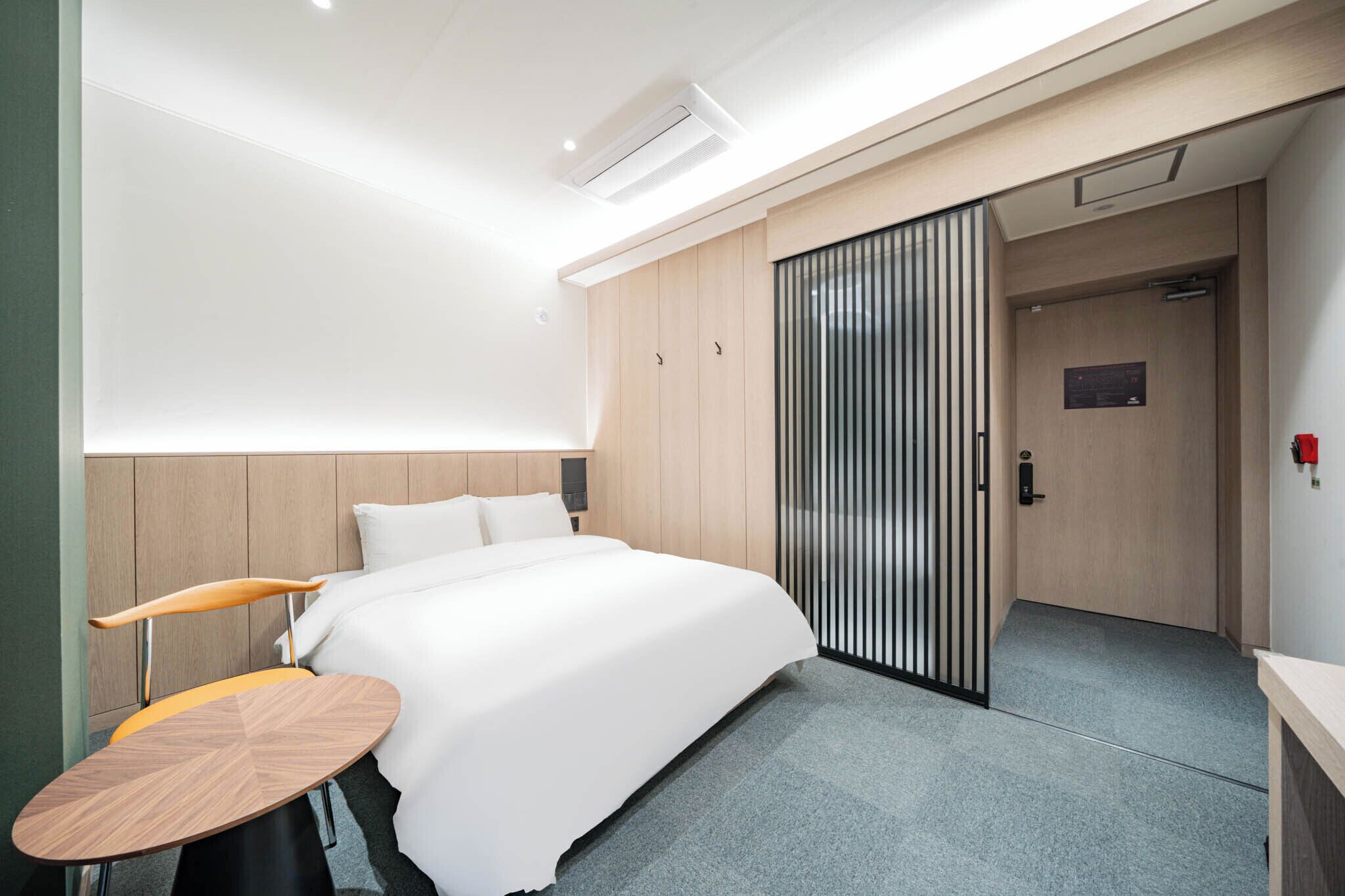Una habitación de hotel moderna con una cama grande, una mesita pequeña y un armario con puerta corredera.