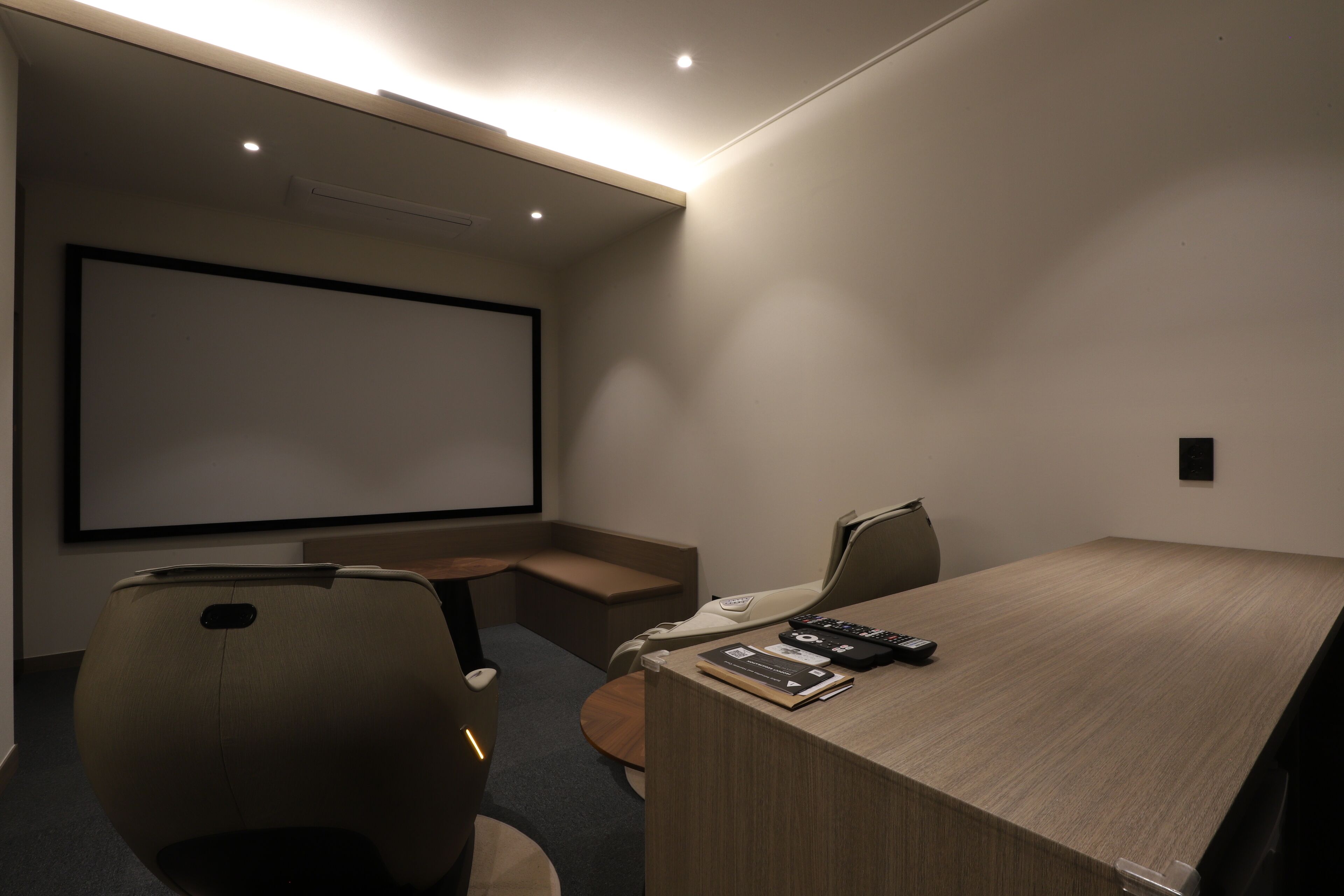 Un salón de conferencias con una pantalla grande, una mesa de madera y dos sillas.
