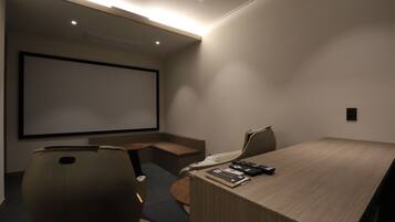 Un salón de conferencias con una pantalla grande, una mesa de madera y dos sillas.