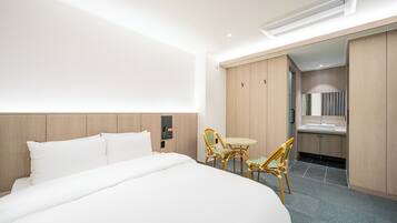 A modern hotel room with a large bed, a small dining table with chairs, a bathroom with a mirror and sink, and wooden paneling on the walls.