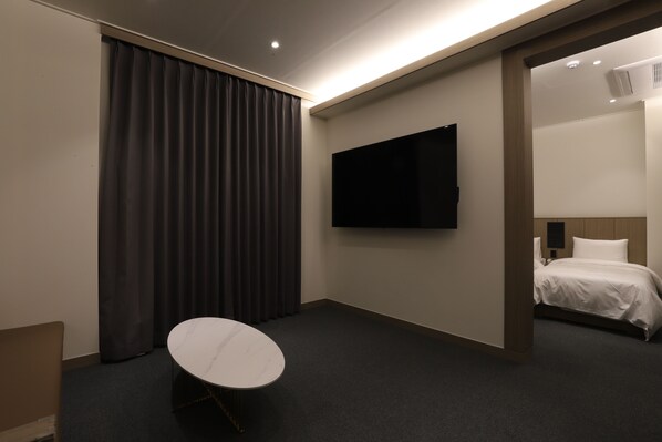 A hotel room with a bed, a TV mounted on the wall, a small round table, and a dark curtain.