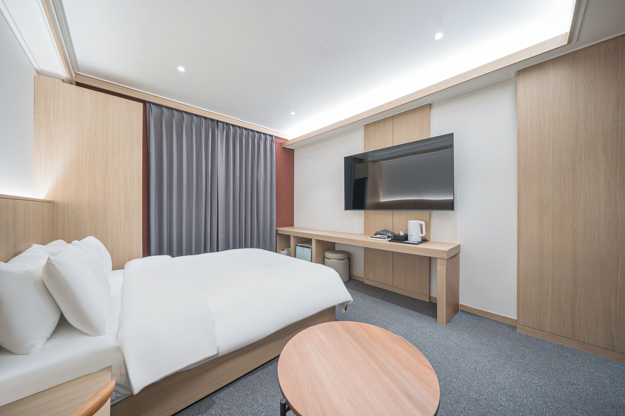 A modern hotel room with a bed, a desk, a flat-screen TV, and a small round table.