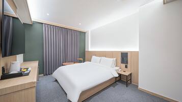 A modern hotel room with a large bed, a desk with a computer, a small table, and a large window with curtains.