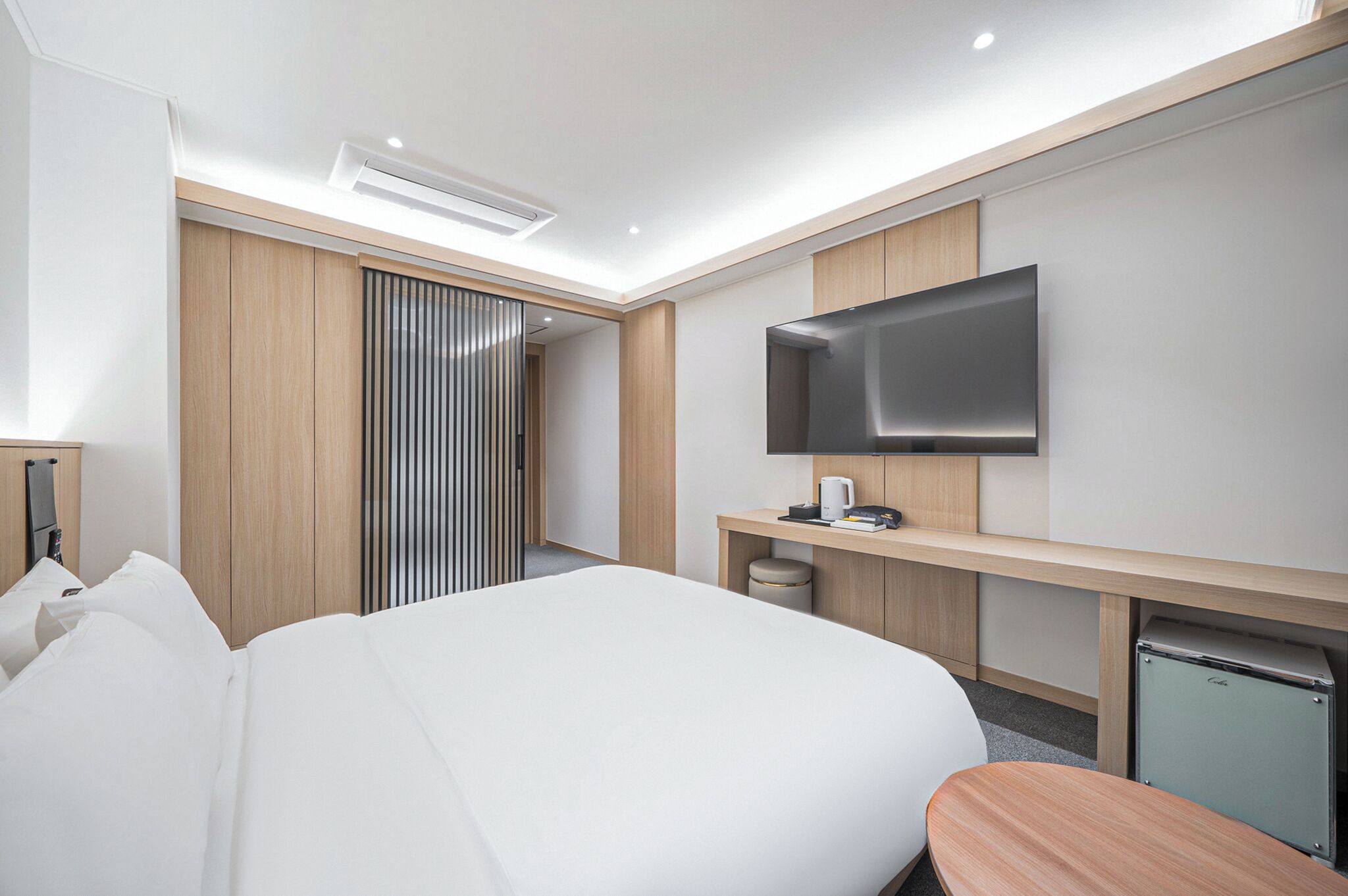 Una habitación de hotel moderna con una cama grande, un televisor montado en la pared, un escritorio con una silla y una pequeña cocina.