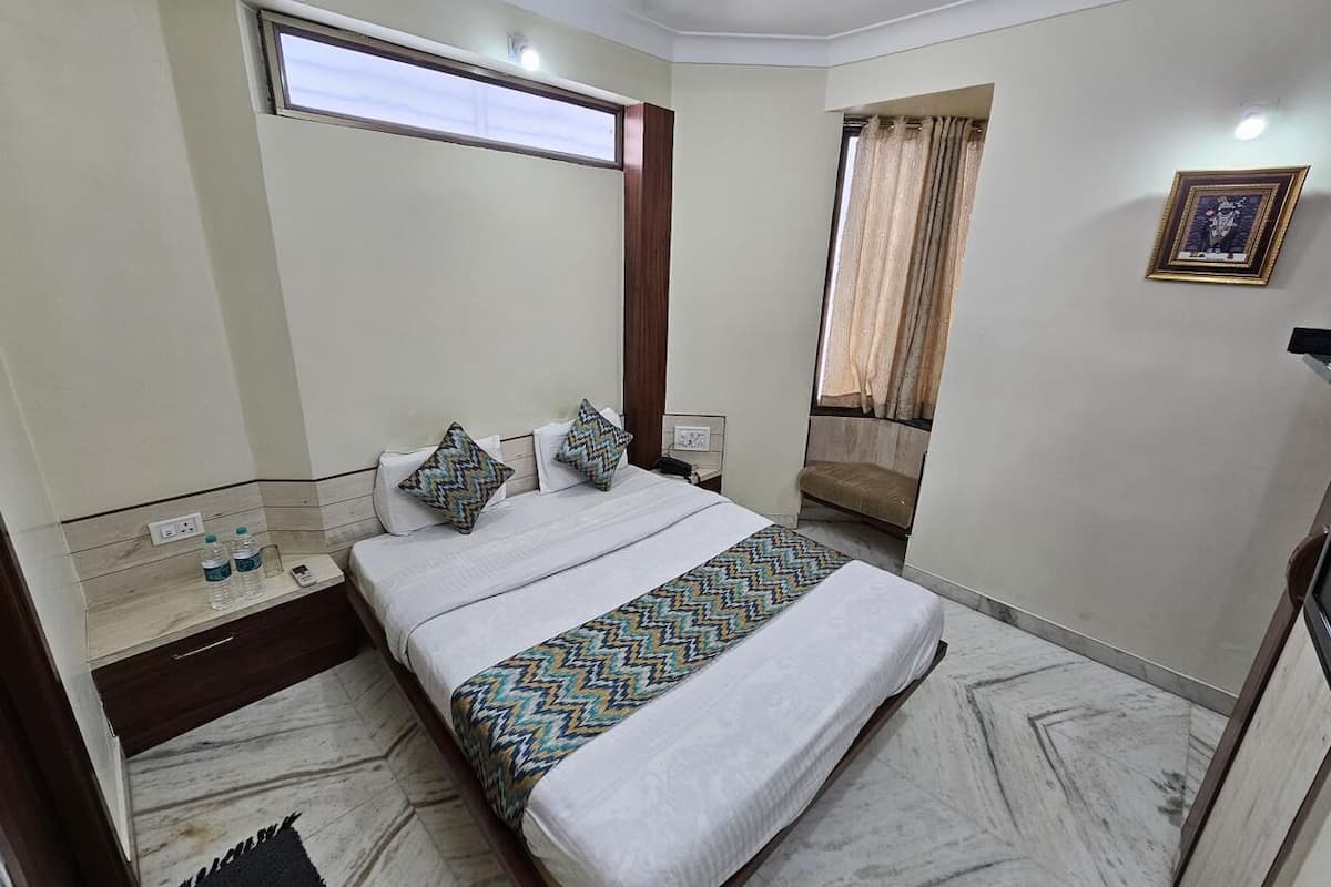A hotel room with a bed, bedside table, nightstand, and a window with curtains.