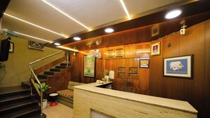 A reception area with a wooden reception desk, a staircase, and framed artwork on the walls. - Hotel Shri Vithalesh (Nathdwara)
