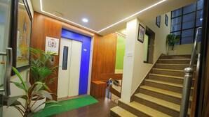 A hotel lobby with a wooden reception desk, a blue elevator, a staircase, and a green mat at the entrance. - Hotel Shri Vithalesh (Nathdwara)