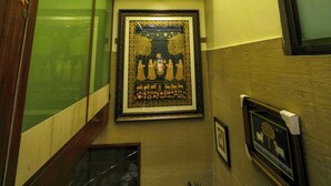 A hallway with a framed artwork depicting a scene with figures and trees, a handrail, and a door with a keyhole. - Hotel Shri Vithalesh (Nathdwara)