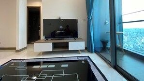 Un soggiorno moderno con una grande TV a schermo piatto su un mobile in legno, un tavolino da caffè in vetro e vista sulla città attraverso un'ampia finestra con tende blu.