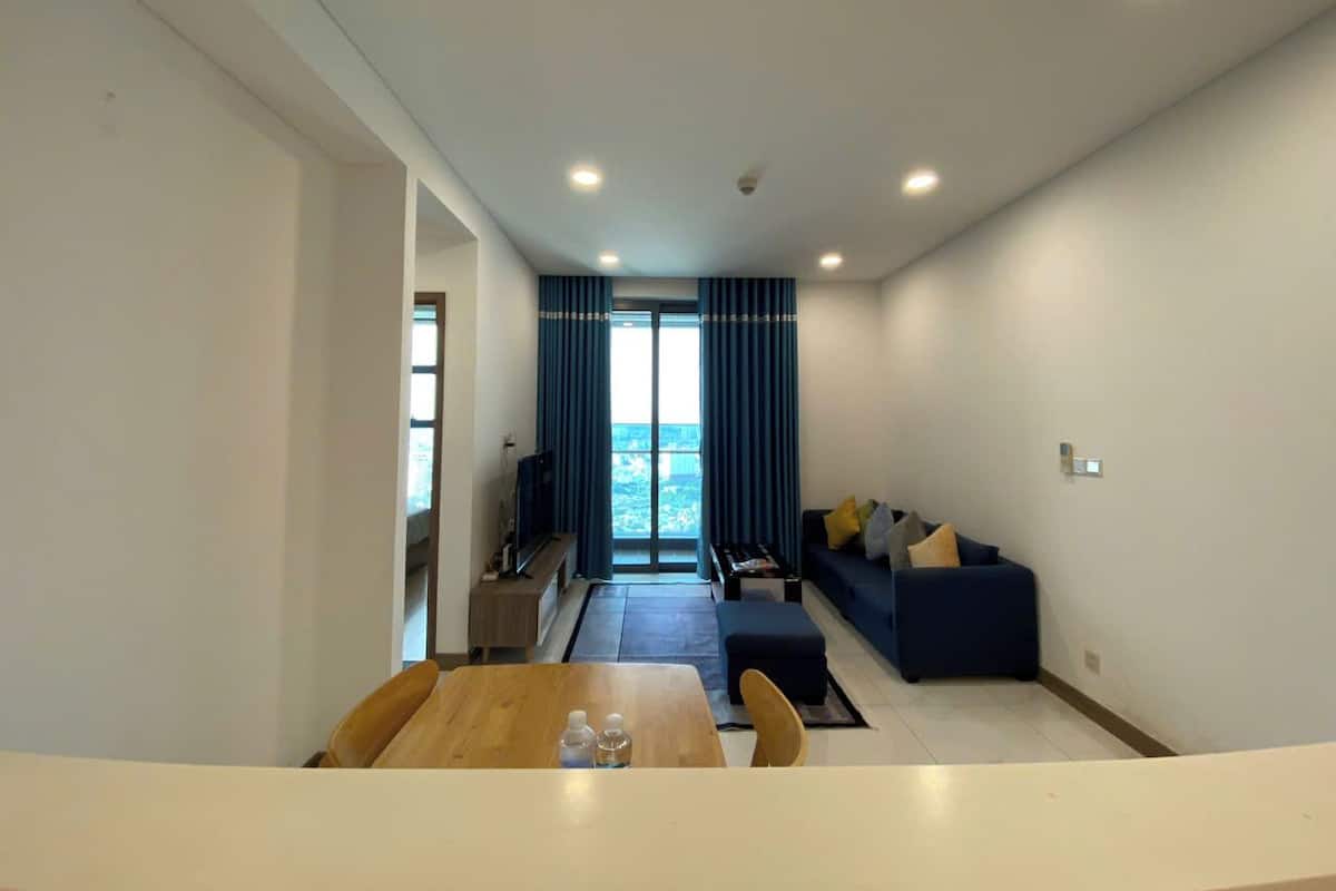 A modern living room with a sofa, a dining table with chairs, and a view through large windows.