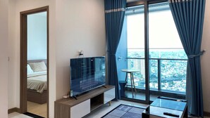 Una camera da letto moderna con un letto, una TV, un tavolino e un balcone con vista sulla città.